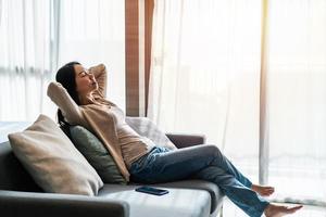 jong vrouw ontspannende Aan sofa Bij knus huis in de ochtend- foto