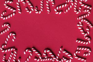 vlak leggen Kerstmis samenstelling met kader van snoep wandelstokken Aan een rood achtergrond. kopiëren ruimte voor tekst foto