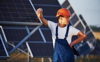 mannetje arbeider in blauw uniform buitenshuis met zonne- batterijen Bij zonnig dag foto