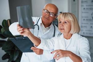 senior Mens en vrouw artsen in wit uniform onderzoekt röntgenstraal van menselijk poten foto