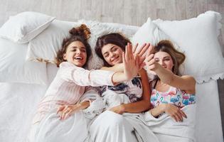 aan het liegen Aan de bed onder de deken samen. gelukkig vrouw vrienden hebben mooi zo tijd Bij pyjama- partij in de slaapkamer foto