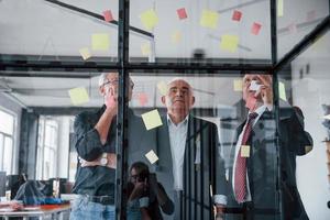 werken met stickers Aan de glas. oud team van ouderen zakenman architecten hebben een vergadering in de kantoor foto