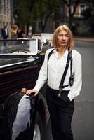 blond vrouw in zwart retro kleren in de buurt oud wijnoogst klassiek auto foto