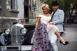 mooi paar in oud fashioned slijtage is in stad met retro auto foto