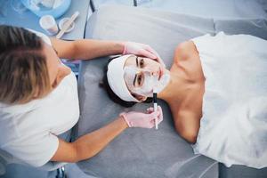 dichtbij omhoog visie van vrouw dat aan het liegen naar beneden in spa salon en hebben gezicht schoonmaak procedure door de masker foto