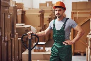 jong mannetje arbeider in uniform is in de magazijn met pallet vrachtauto foto