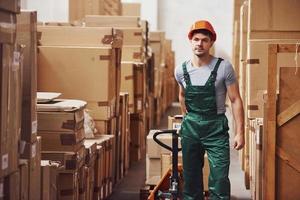 jong mannetje arbeider in uniform is in de magazijn met pallet vrachtauto foto