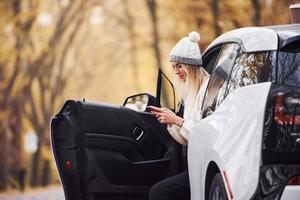 gebruik makend van smartphone. meisje hebben herfst reis door auto. modern merk nieuw auto- in de Woud foto