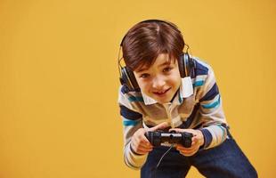 schattig weinig jongen spelen video spel in de studio tegen geel achtergrond foto