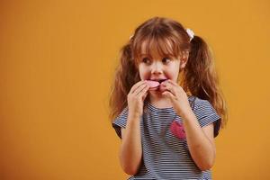 schattig weinig meisje met zoet voedsel in de studio tegen geel achtergrond foto