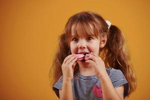 schattig weinig meisje met zoet voedsel in de studio tegen geel achtergrond foto