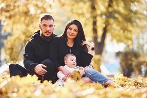 vrolijk familie zit Aan de grond en hebben pret samen met hun kind in mooi herfst park foto