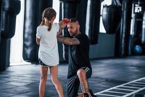 eenvoudig stoten. jong getatoeëerd boksen trainer geeft les schattig weinig meisje in de Sportschool foto