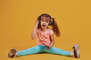 portret van schattig weinig meisje in hoofdtelefoons en met telefoon in de studio tegen geel achtergrond foto