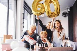 ballonnen met aantal 60. senior vrouw met familie en vrienden vieren een verjaardag binnenshuis foto