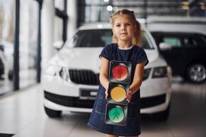 portret van schattig weinig meisje dat houdt verkeer lichten afbeelding in handen in auto- salon foto