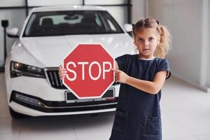 portret van schattig weinig meisje dat houdt weg teken in handen in auto- salon foto