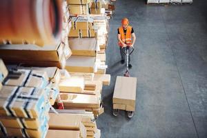 jong mannetje arbeider in uniform is in de magazijn voortvarend pallet vrachtauto foto