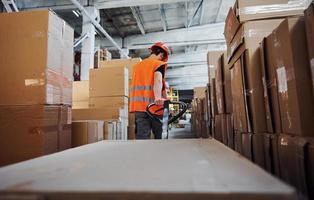 jong mannetje arbeider in uniform is in de magazijn voortvarend pallet vrachtauto foto