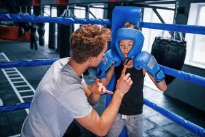 jong boksen trainer is helpen weinig jongen in beschermend slijtage Aan de ring tussen de rondes foto