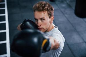 jong Mens in wit overhemd en boksen beschermend handschoenen aan het doen opdrachten in Sportschool foto