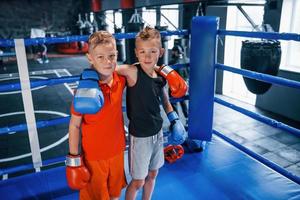 portret van twee jong jongens in beschermend handschoenen staand samen Aan boksen ring foto