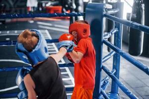 twee jongens in beschermend uitrusting hebben sparren en vechten Aan de boksen ring foto