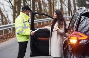 mannetje Politie officier in groen uniform pratend met vrouw eigenaar van de auto Aan de weg foto