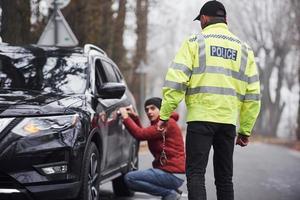 Politie officier in groen uniform gevangen auto- diefstal Aan de weg foto