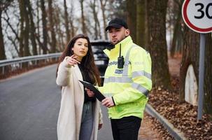 mannetje Politie officier in groen uniform pratend met vrouw eigenaar van de auto Aan de weg foto