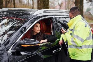 mannetje Politie officier in groen uniform pratend door radio zender in de buurt auto met vrouw bestuurder foto