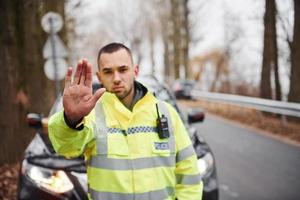 mannetje Politie officier in groen uniform tonen hou op gebaar in de buurt voertuig foto