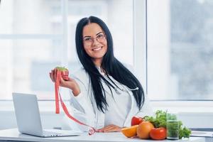 vrouw voedingsdeskundige in wit jas Holding appel met meten plakband foto