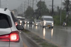 achterzijde sid van wit auto Aan de weg met wazig van rem licht. nat weg voorwaarden gedurende regenachtig seizoen. wazig beeld van een auto Aan de tegenover lens met lichten Aan. foto