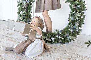 een jong vrouw met blond haar- en een weinig dochter met een Kerstmis lauwerkrans. nieuw jaar begrip, kerstmis decoraties foto