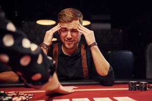 elegant jong Mens zit in casino en voelt slecht omdat verliest poker spel foto