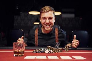 gelukkig elegant jong Mens zit in casino en vieren zijn zege in poker spel foto