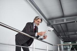 senior zakenman in pak en stropdas met grijs haar- en baard houdt documenten in handen foto