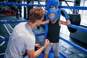 jong boksen trainer is helpen weinig jongen in beschermend slijtage Aan de ring tussen de rondes foto