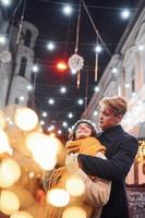 gelukkig jong paar in warm kleren is Aan Kerstmis versierd straat samen foto