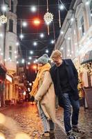 schattig paar in warm kleren is Aan Kerstmis versierd straat glimlachen en hebben pret foto