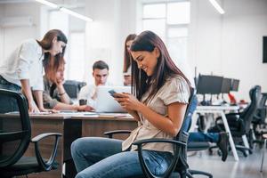 knap vrouw met telefoon is in de kantoor. groep van mensen werken Bij project achter foto