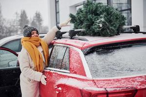 positief jong meisje staand in de buurt auto met groen Kerstmis boom Aan top foto