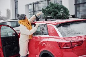 positief jong meisje staand in de buurt auto met groen Kerstmis boom Aan top foto