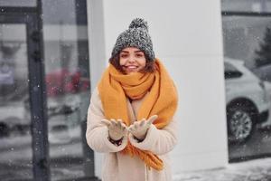 vrolijk jong meisje glimlachen staand en glimlachen buitenshuis. sneeuw is vallend foto