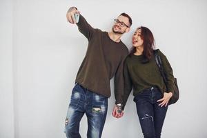 vrolijk multi etnisch paar in gewoontjes kleren maken selfie binnenshuis in de studio tegen wit achtergrond foto