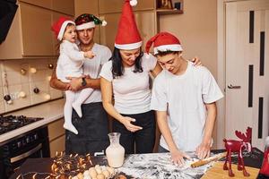 feestelijk familie in Kerstmis hoeden hebben pret Aan de keuken en voorbereidingen treffen voedsel foto