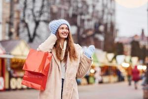 jong meisje in warm kleren met boodschappen doen Tassen in handen hebben een wandelen buitenshuis in de stad foto