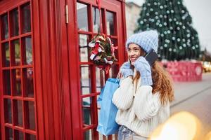 jong meisje in warm kleren hebben een wandelen buitenshuis in de stad in de buurt rood telefoon station foto