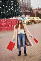 jong meisje in warm kleren met boodschappen doen Tassen in handen hebben een wandelen buitenshuis in de stad foto